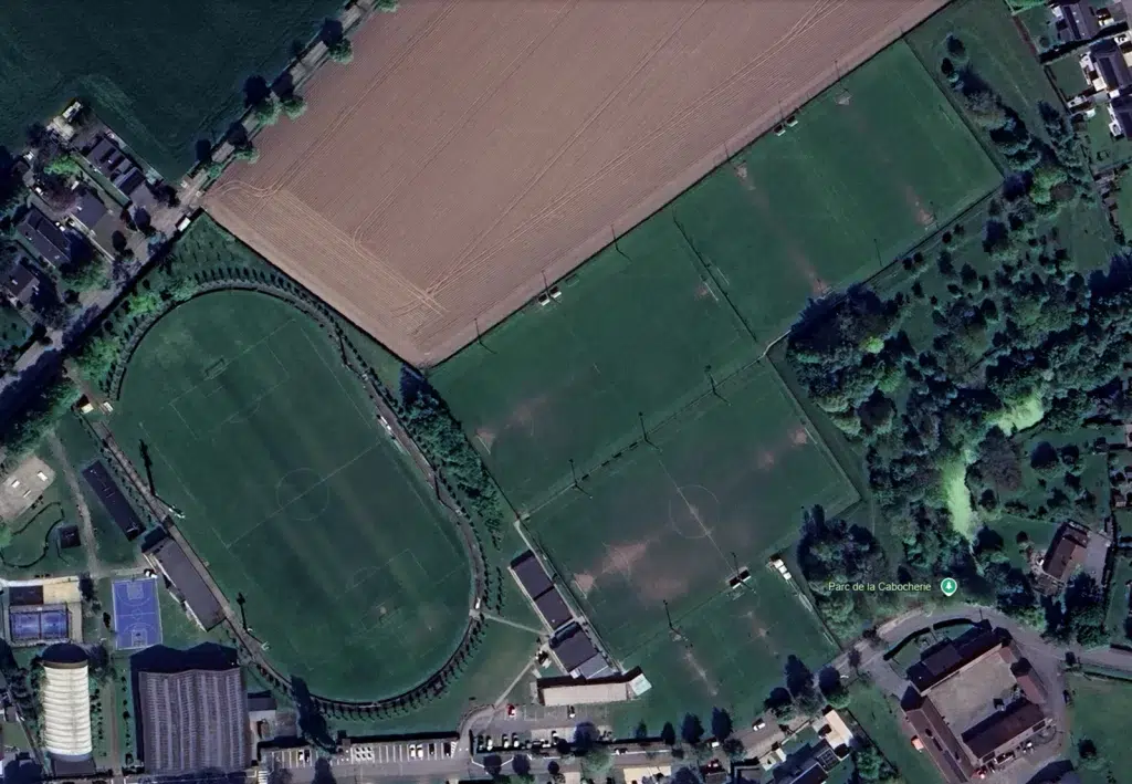 Aerial view of a park showing a circular running track around a soccer field and several adjacent green fields with trees and nearby buildings