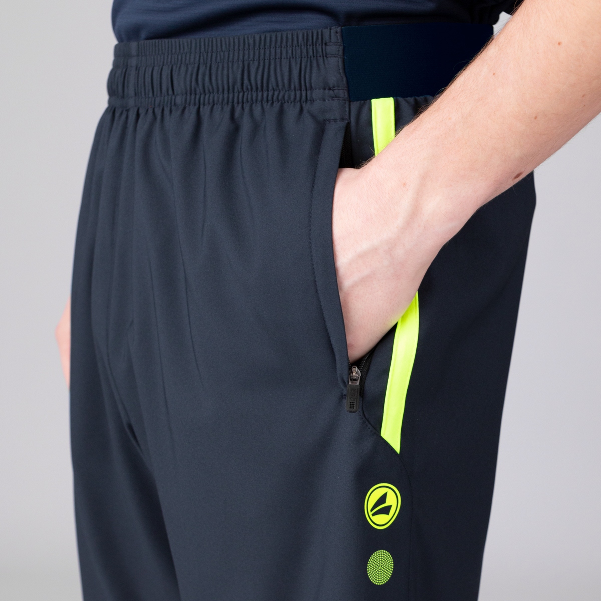 Close-up of dark athletic pants showing a side zip pocket with a bright neon yellow trim and logo near the leg area.